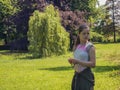 Sad lonely caucasian teenage girl in the park surrounded by trees on the background