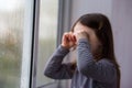 Sad lonely child girl with brown hair cries near the window. raindrops on glass. soft focus Royalty Free Stock Photo