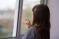 Sad lonely child girl with brown hair looks out the window. raindrops on the glass. back view Royalty Free Stock Photo