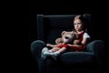 Sad, lonely child sitting in armchair and holding teddy bear Royalty Free Stock Photo