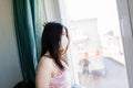 Sad lonely girl isolated at home in protective sterile medical mask on her face looking at window, bored woman because of Chinese