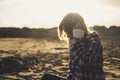 Sad lonely girl sit down at the beach during the dusk of the sunset - golden colors and sand in background for people love to be