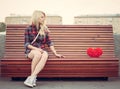 Sad lonely girl sitting on a bench near to a big red heart