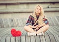 Sad lonely girl sitting on wood planks near to a big red heart Royalty Free Stock Photo