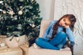 Sad little girl sitting in chair by Christmas tree during coronavirus pandemic. Stay at home for Christmas holidays Royalty Free Stock Photo