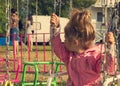 Sad lonely little girl sitting on swing in a park, looks for her mum Royalty Free Stock Photo