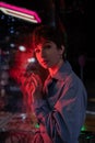 Sad lonely woman in red neon light leaning on shop window on street at night, looking at camera