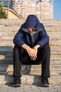 Sad lonely troubled teenage boy with hands down sitting on steps outdoors