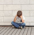 Sad, lonely, unhappy, disappointed child sitting alone on the ground. Boy holding his head, look down. Outdoor Royalty Free Stock Photo