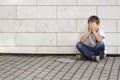 Sad, lonely, unhappy, disappointed child sitting alone on the ground. Boy holding his head, look down. The tablet pc Royalty Free Stock Photo