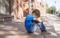 Sad, lonely, unhappy, disappointed child sitting alone on the ground. City background. Outdoor Royalty Free Stock Photo