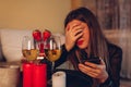 Sad woman crying at home by romantic table setting with wine glasses. Breaking up on Valentine& x27;s Day via phone call Royalty Free Stock Photo