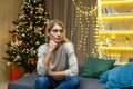 Sad and lonely young beautiful woman sitting at home on the sofa near the Christmas tree Royalty Free Stock Photo