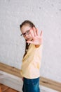 Sad long hair tweens girl in glasses pulling hand towards camera on white wall background