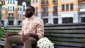 Sad male nervously waiting for girl, sitting park bench with flowers, blind date Royalty Free Stock Photo