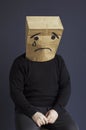 A sad man in a black turtleneck with a bag on his head, with a drawn crying emoticon, sits on a chair.