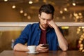 Sad man with coffee and smartphone at restaurant Royalty Free Stock Photo
