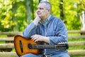 Sad man with guitar in park on bench Royalty Free Stock Photo