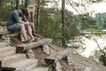 A sad man with a guitar sits on a wooden bench on a hill overlooking the lake on a summer evening