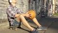 Sad man in headphones sitting on skateboard, thinking about life, holding ball Royalty Free Stock Photo