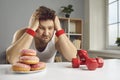 Sad man looking at dumbbells and donuts choosing between healthy and unhealthy lifestyle