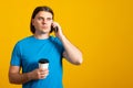 Sad man with a serious  expression, talking on a cell phone, drinking coffee take away, wearing a blue t-shirt. Copy space Royalty Free Stock Photo