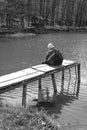 A sad man is sitting alone on pier by the lake. Forest black and white. hood on his head. backpack. in hands hold phone. Emotions Royalty Free Stock Photo