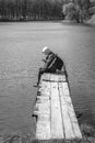 A sad man is sitting alone on pier by the lake. Forest black and white. hood on his head. backpack. in hands hold phone. Emotions Royalty Free Stock Photo