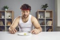 Sad man on strict diet sitting at table and looking at tiny piece of apple on plate