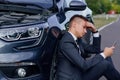 Sad man use smartphone sitting on road near the broken car opened the hood, calling car assistance services, Royalty Free Stock Photo