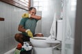 Sad man wearing gloves over his nose cleaning smelly toilet Royalty Free Stock Photo