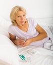 Sad mature woman laying in bed with pills Royalty Free Stock Photo