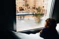 Sad and melancholic boy looks through a window in his apartment during his confinement