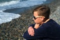 Sad melancholy teenager boy sitting on sea pebble beach looking at waves. Royalty Free Stock Photo