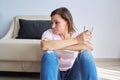 Sad middle aged woman sitting at home on the floor with glass of water Royalty Free Stock Photo