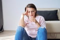 Sad middle aged woman sitting at home on the floor with glass of water Royalty Free Stock Photo