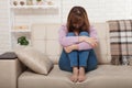 Sad middle aged woman sitting on sofa with clamped knees and crying. Home background Royalty Free Stock Photo