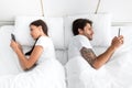 Sad millennial european couple chatting on smartphones back to back, lying on bed in bedroom Royalty Free Stock Photo
