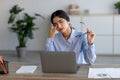 Sad millennial indian female employee suffer from headache, fatigue rubs eyes at workplace with laptop Royalty Free Stock Photo