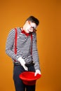 Sad mime in vest holding empty red hat on orange background Royalty Free Stock Photo