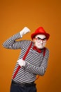 Sad mime with white face in red hat and striped t-shirt on blank orange background Royalty Free Stock Photo