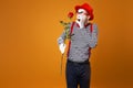 Sad mime with white face in red hat and striped t-shirt holding rose on empty orange background Royalty Free Stock Photo