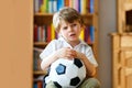 Sad and not happy little kid with football about lost football or soccer game. child after watching match on tv