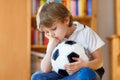 Sad and not happy little kid with football about lost football or soccer game. child after watching match on tv Royalty Free Stock Photo