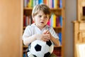 Sad and not happy little kid with football about lost football or soccer game. child after watching match on tv Royalty Free Stock Photo