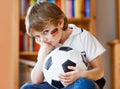 Sad and not happy little kid with football about lost football or soccer game. child after watching match on tv