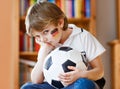 Sad and not happy little kid with football about lost football or soccer game. child after watching match on tv Royalty Free Stock Photo