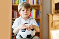 Sad and not happy little kid with football about lost football or soccer game. child after watching match on tv Royalty Free Stock Photo