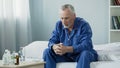 Sad old man sitting in bed and looking at pills, medication and healthcare Royalty Free Stock Photo