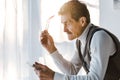 Sad pensioner holding glasses and looking at photo in photo frame while sitting